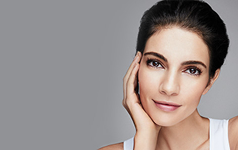 Model with hair pulled back resting chin in hand against a gray background. 