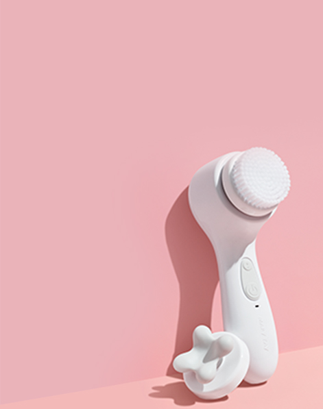 Mary Kay Skinvigorate Sonic Skin Care System and Skinvigorate Sonic Facial Massage Head standing against pink background.