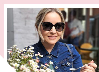 Image of woman outside smiling wearing sunglasses and holding a bouquet of small flowers