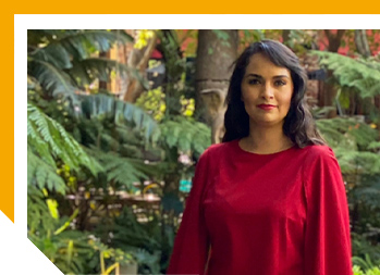 Image of woman outside smiling in red shirt with greenery in the background