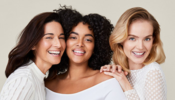 A picture of a mature Latina, a curvy black woman, and a blonde white woman with glowing skin smiling and laughing