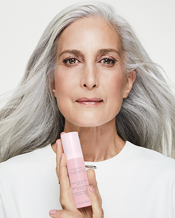 A mature white woman with gray hair holding TimeWise Tone Correcting Serum