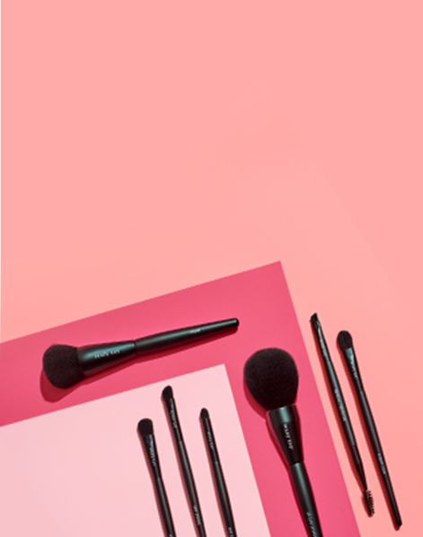 A mix of Mary Kay makeup brushes on a pink geometric background