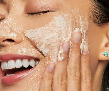 An Asian woman smiling and exfoliating with Mary Kay Naturally Exfoliating Powder.