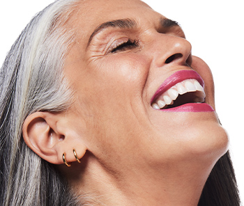 Grey-haired woman wearing hot pink lipstick laughing with her head tossed back