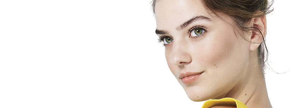 Watch the video to see how to create your most flawless face using Mary Kay products and tools. Image shows a woman looking up in the right corner. The new Mary Kay blending sponge is held to the left upper corner of her face by a hand. 