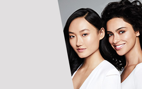Two dark-haired women pose side-by-side in white tops.