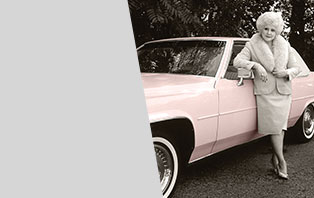 Mary Kay Ash leans against a classic pink Cadillac while wearing a pink fur-trimmed dress suit.