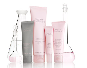 Four Mary Kay products from the new TimeWise Miracle Set 3D skin care regimen are shown in pink and grey packaging in front of glass beakers filled with pink liquid. The set includes the 4-in-1 Cleanser, the Day Cream SPF 30, the Night Cream and the Eye Cream.