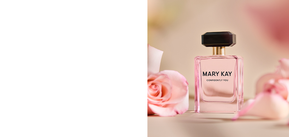 The light pink perfume bottle with a black cap is surrounded by roses on a tabletop.
